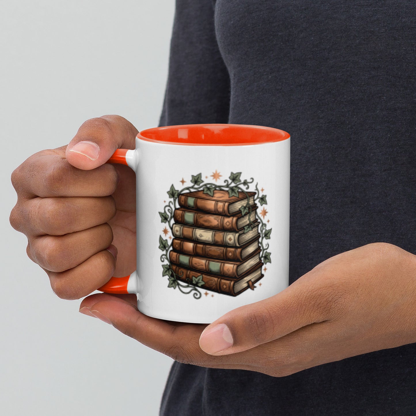 Stacked books and ivy design on a white ceramic mug with orange rim and handle, 11 oz, left view