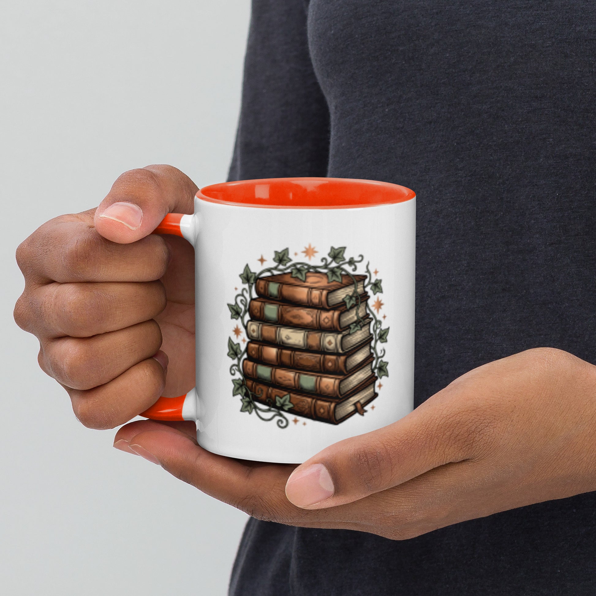 Stacked books and ivy design on a white ceramic mug with orange rim and handle, 11 oz, left view
