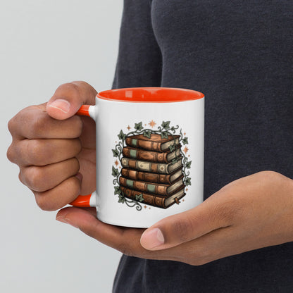 Stacked books and ivy design on a white ceramic mug with orange rim and handle, 11 oz, left view