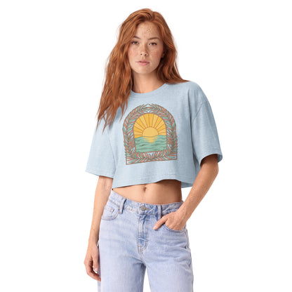 Retro sunrise and ocean arch framed in botanicals on a light washed denim garment-dyed cropped tee, front view
